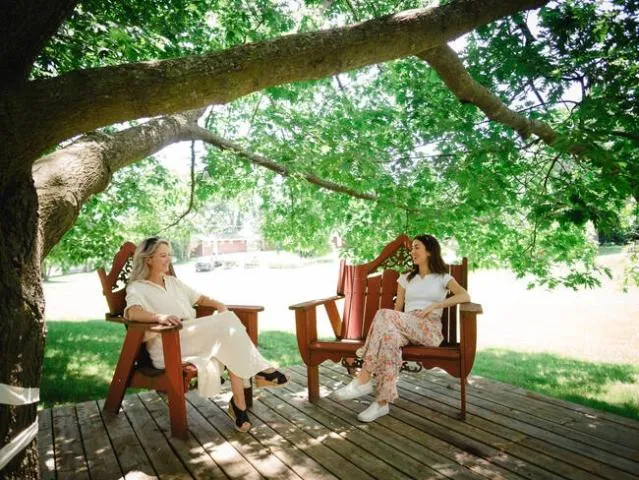 2 people sitting in chairs outside in the shade of a tree