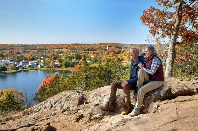2 people sitting atop a small mountain overlooking a lake