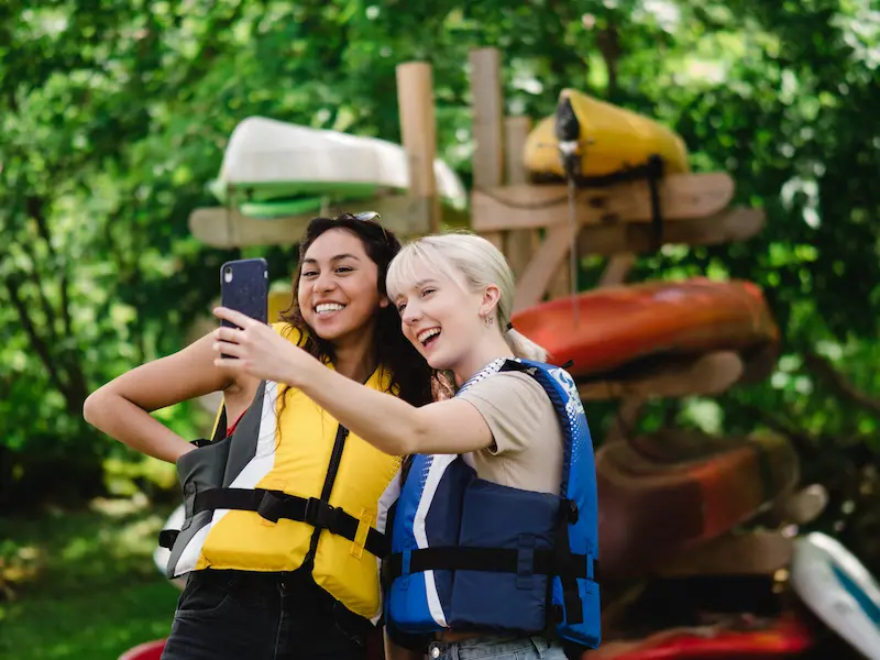 two girls taking selfie in front of kayaks